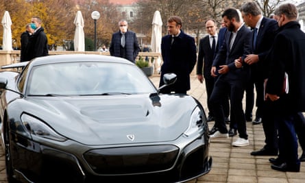 Macron, en pardessus, regarde une supercar noire garée dehors sur une terrasse, avec un groupe de passants dont Mate Rimac